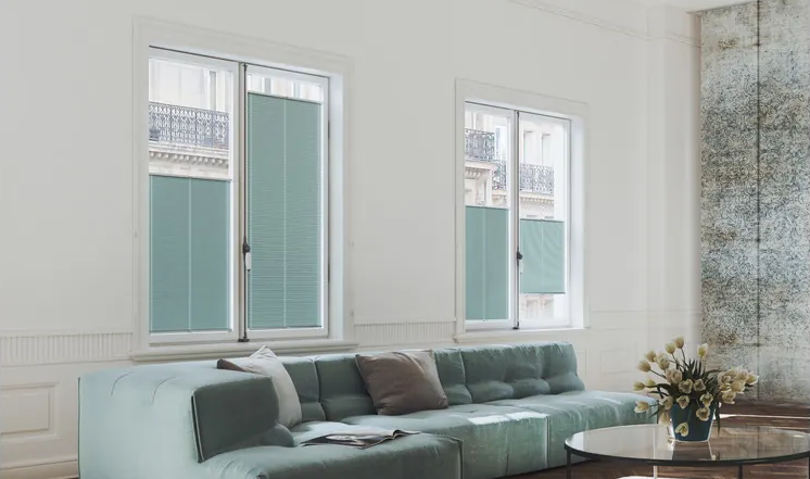 Plissees an vier Fenstern komplementieren die Farbe eines mintgrünen Sofas in einem Wohnzimmer.