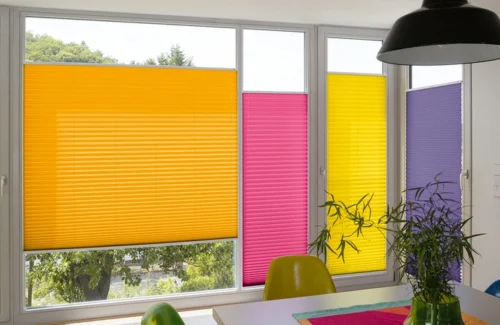 Verschiedenfarbene Plissees beschatten aneinanderliegende Fenster verschiedener Größen.
