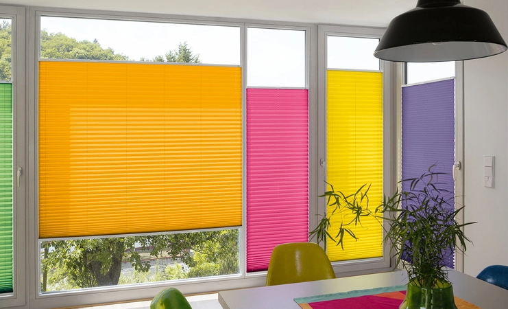 Verschiedenfarbene Plissees beschatten aneinanderliegende Fenster verschiedener Größen.