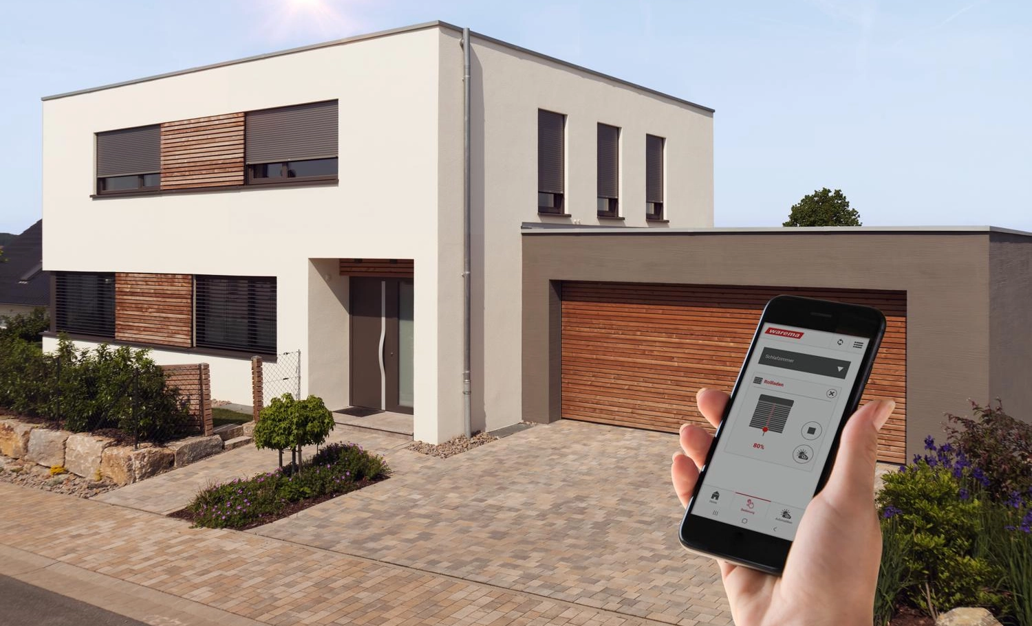 Ein Handy mit WAREMA-Steuersoftware vor einem Haus mit Garagentor und Außenliegendem Sonnenschutz an den Fenstern.