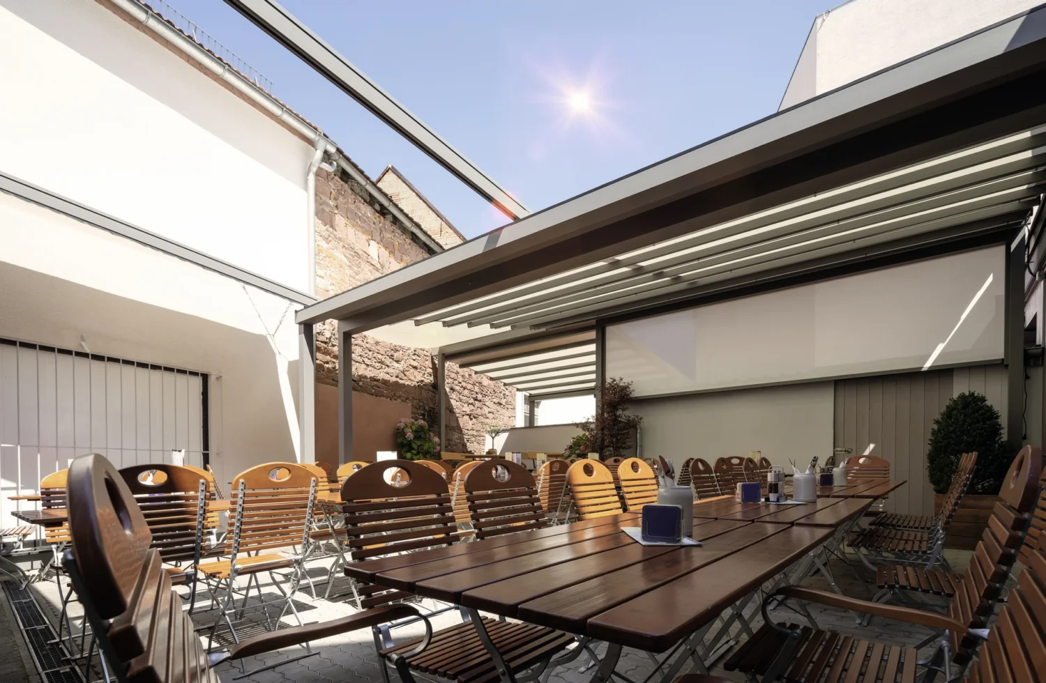 Sonniger Biergarten mit modernen Überdachungen und Holzstühlen